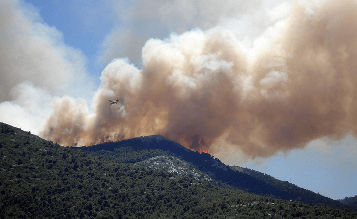 An aircraft flies over a mountainside wildfire in Ventura County, releasing thick smoke into the sky—illustrating the region’s increasing wildfire risk amid rising temperatures and prolonged droughts.