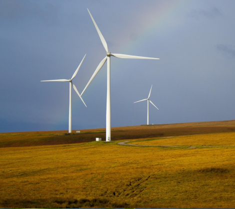 Tall white wind turbines stand on an open grassy landscape under a cloudy sky, symbolizing cleaner air and reduced pollution through sustainable practices.